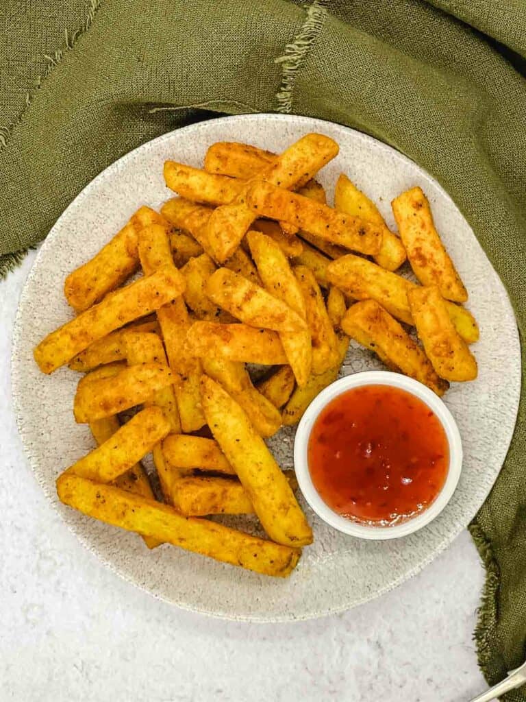A plate filled with masala fries and a sweet chilli dipping sauce.