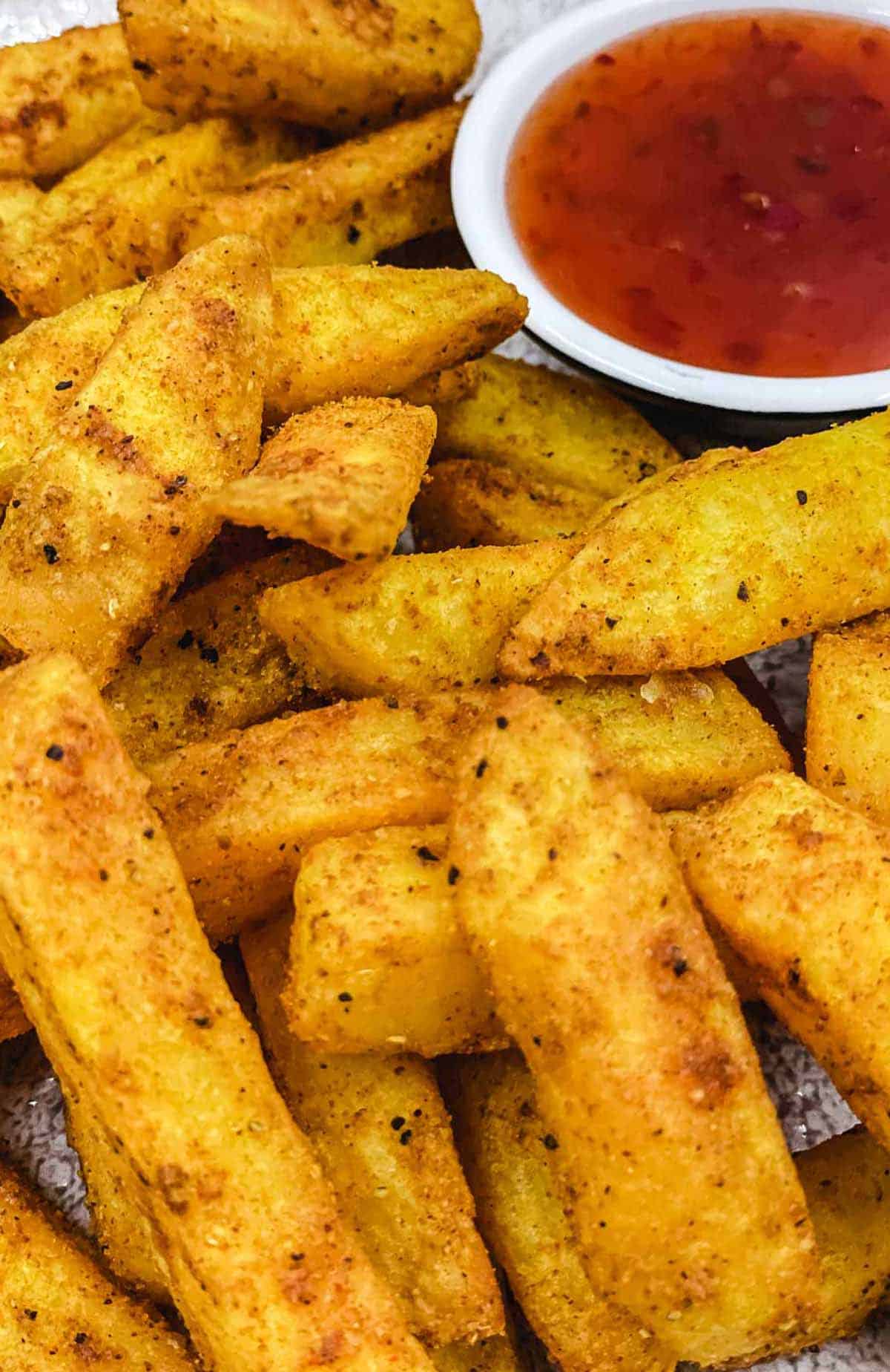 A plate of air fryer masala fries with sweet chili sauce.