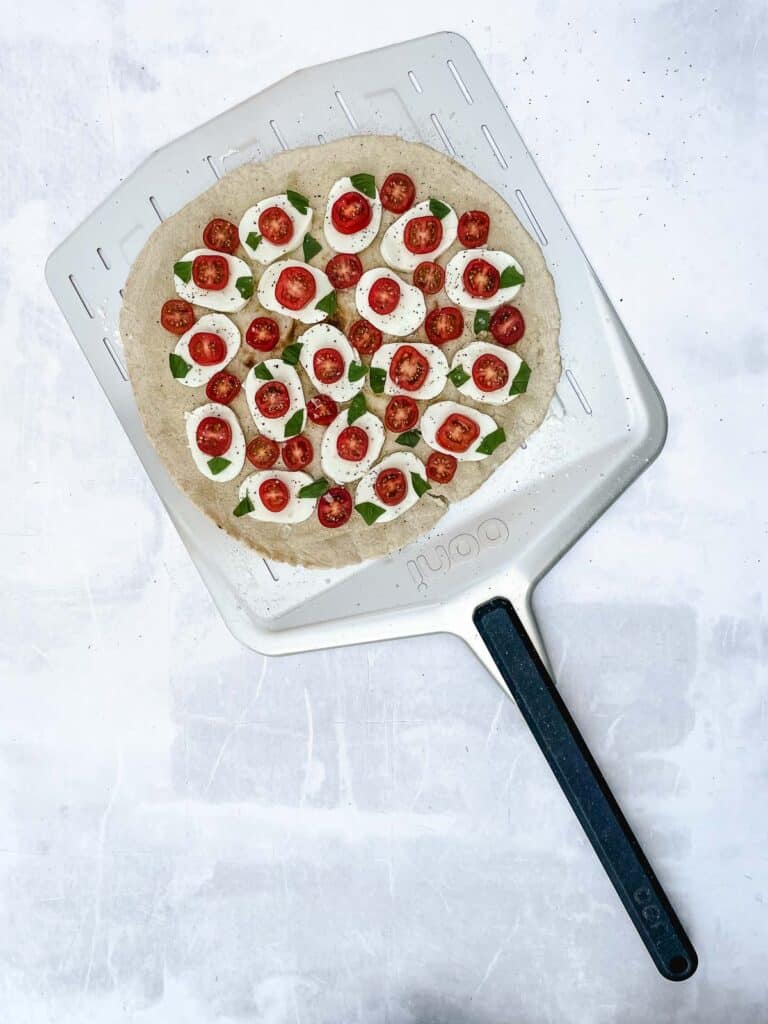 Uncooked Caprese pizza on a pizza paddle.