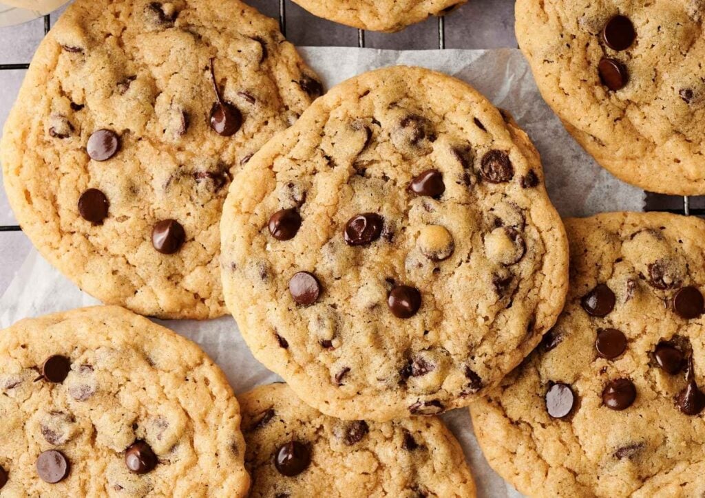 Close-up of several freshly baked chocolate chip cookies on a cooling rack, highlighting their golden-brown edges and melty chocolate chips.