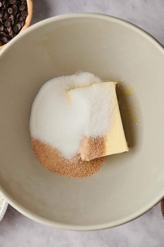 A bowl containing soft butter, white granulated sugar, and light brown sugar, ready to be mixed for chocolate chip cookies.