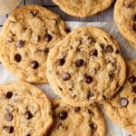 A batch of gooey chocolate chip cookies is cooling on a wire rack lined with parchment paper, filling the air with a delightful aroma.