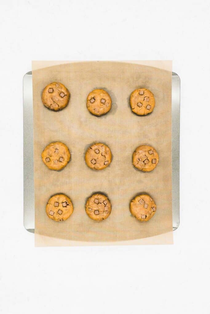 Peanut butter chocolate chip cookie dough balls on a baking sheet, ready to cook.