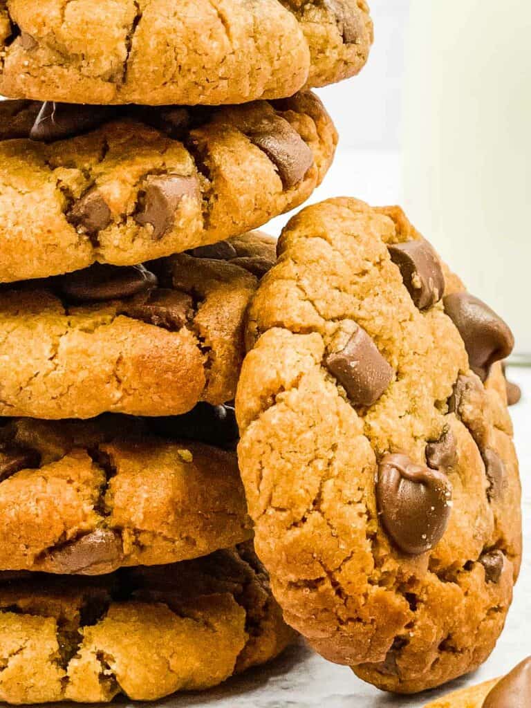 Peanut butter chocolate chip cookies staked, with one cookie resting against the stack.