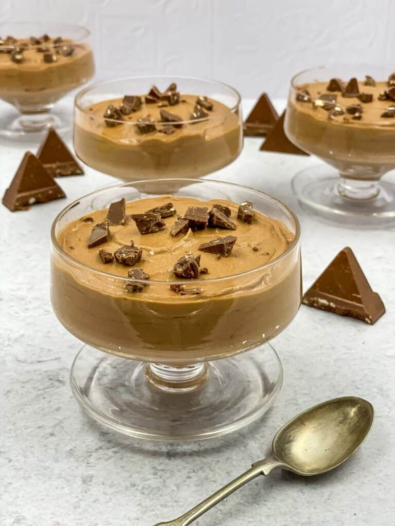Toblerone mousse in serving bowls, with triangles of chocolate and a spoon.