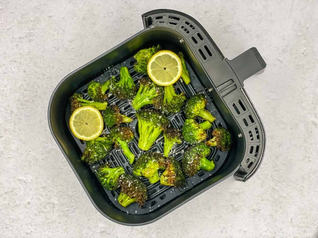 Broccoli florets, lemon slices, and Parmesan cheese in an air fryer basket.