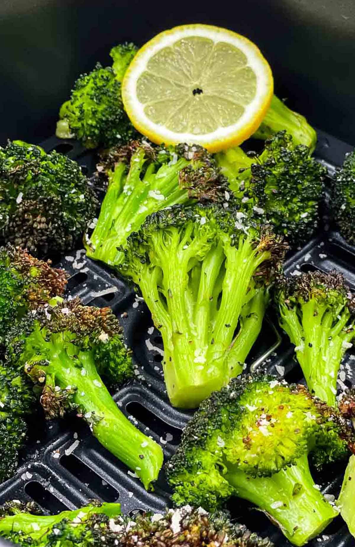 Freshly cooked broccoli with a lemon slice in an air fryer basket.