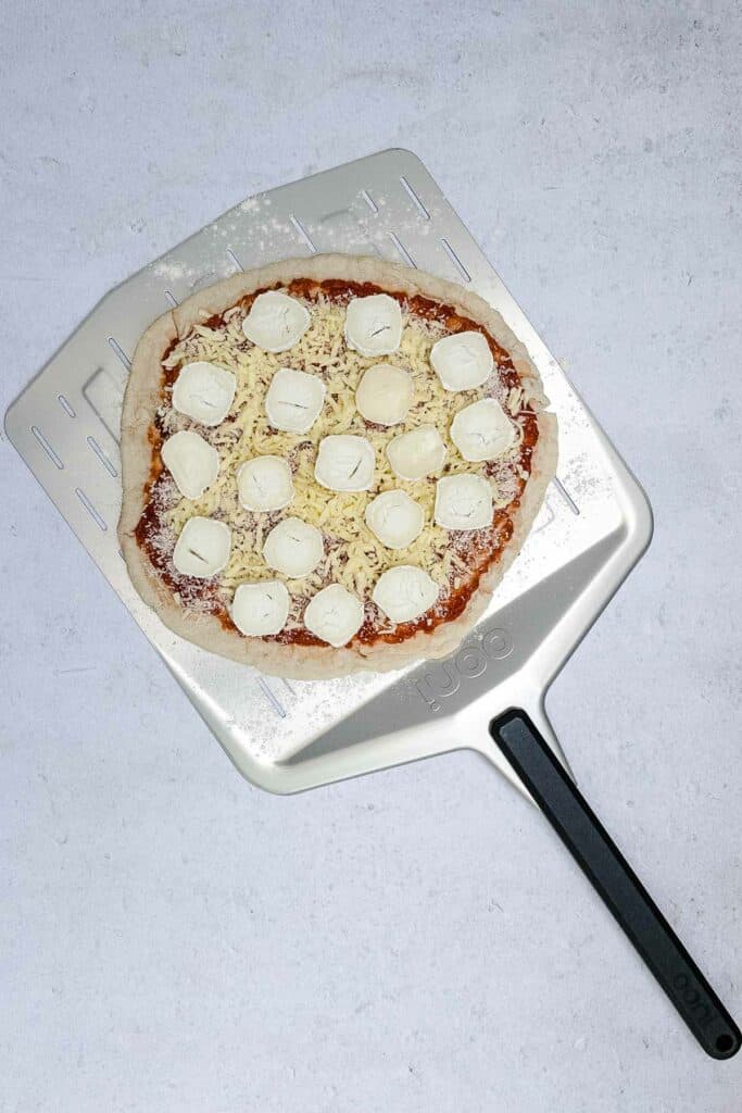 Cheese pizza on a pizza paddle ready to go into the oven.