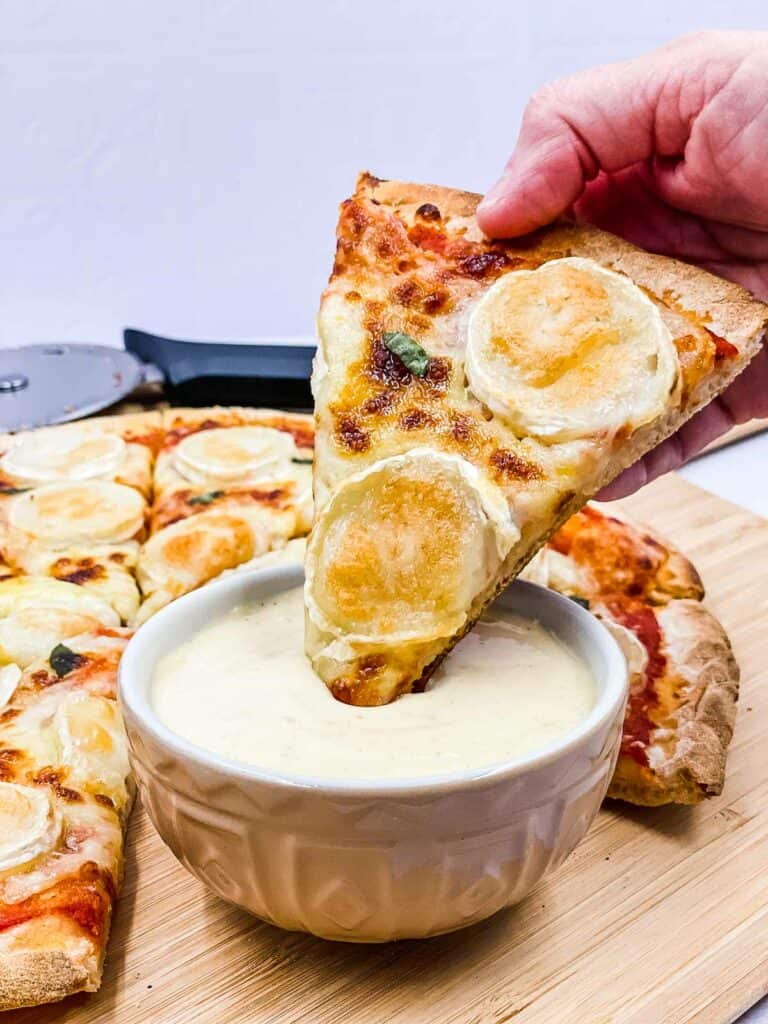 Someone dipping a slice of cheese pizza into a dipping sauce.