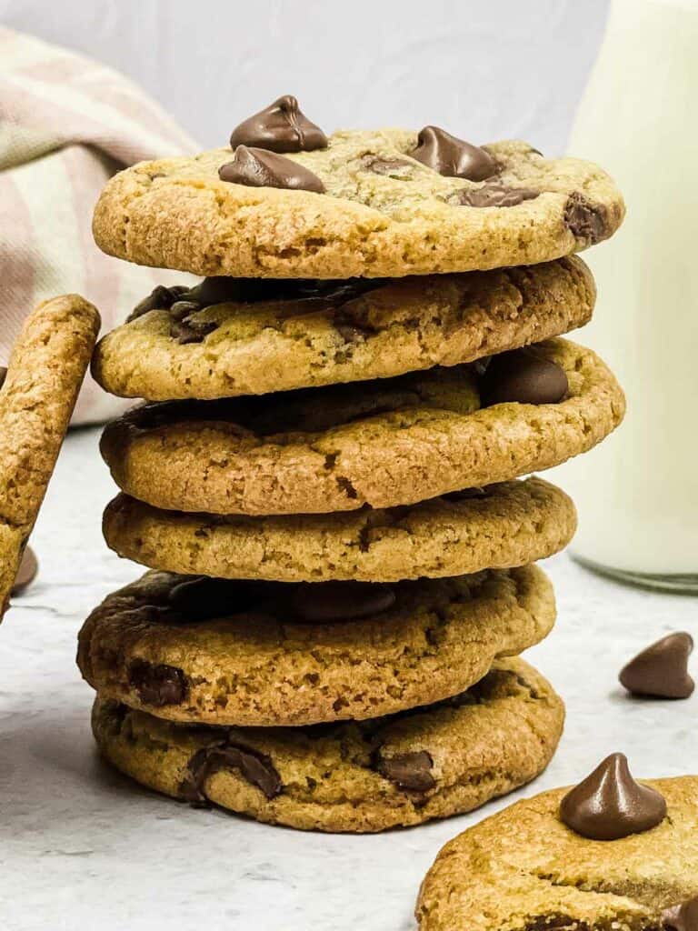 A stack of chocolate chip cookies with a bottle of milk and a couple of cookies around it.