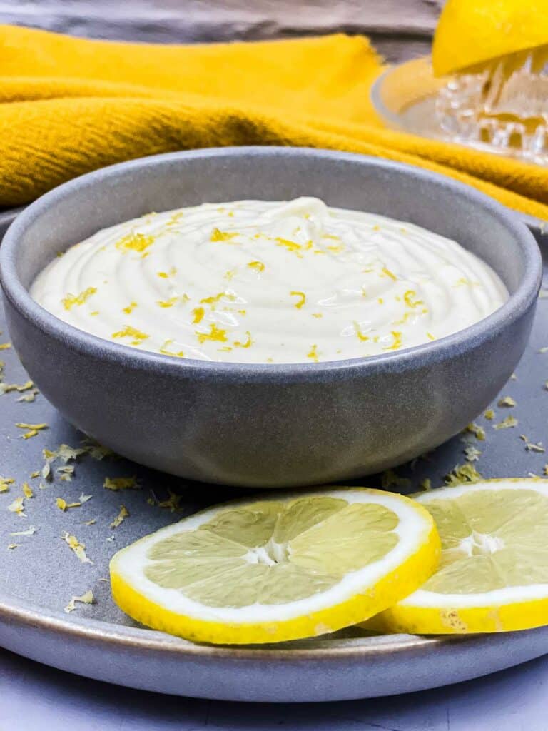 A bowl of lemon aioli with lemon zest and slices of lemon.