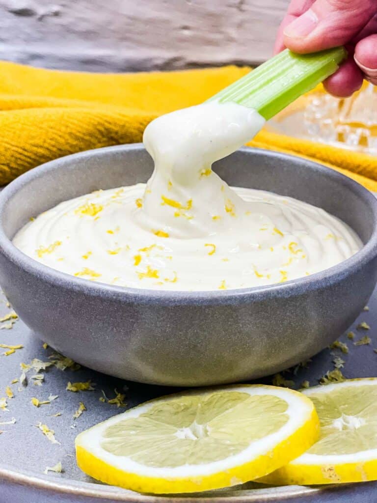 Someone dipping celery into a bowl of aioli made with lemon.