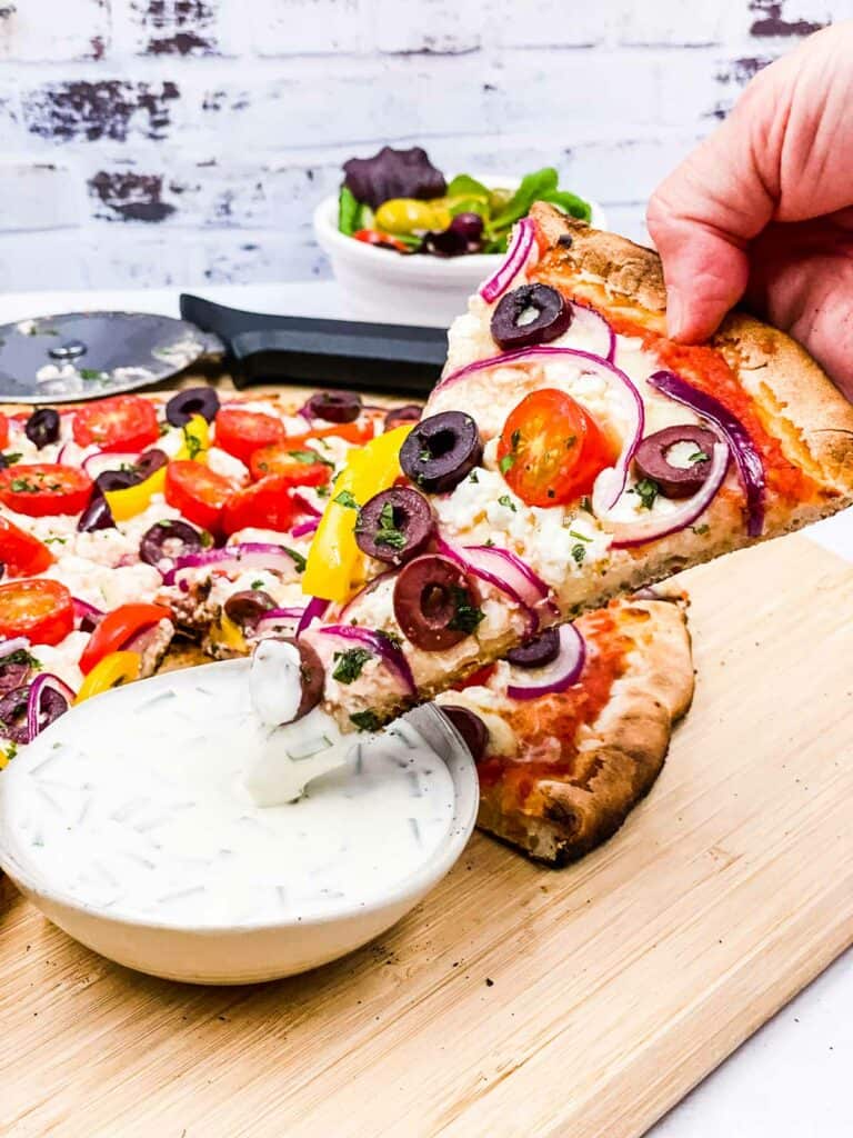 Someone dipping Greek style pizza in a pizza dip.