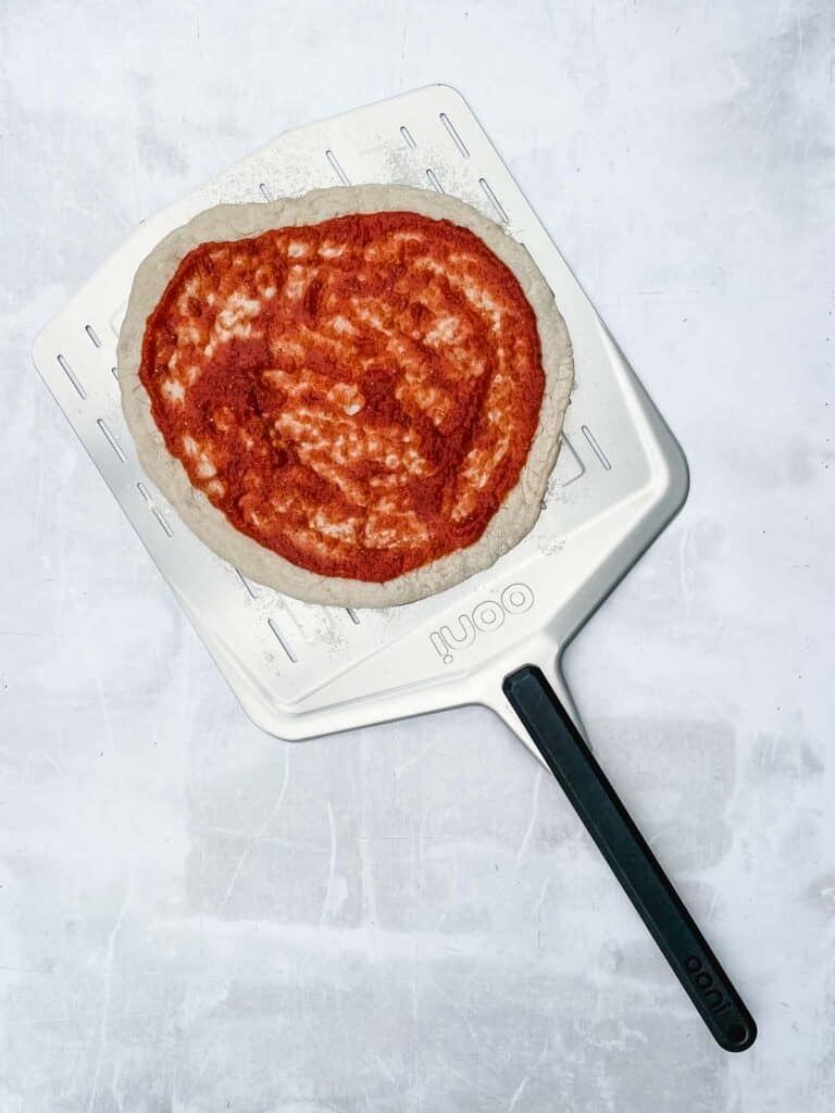 A pizza crust with pizza sauce on.