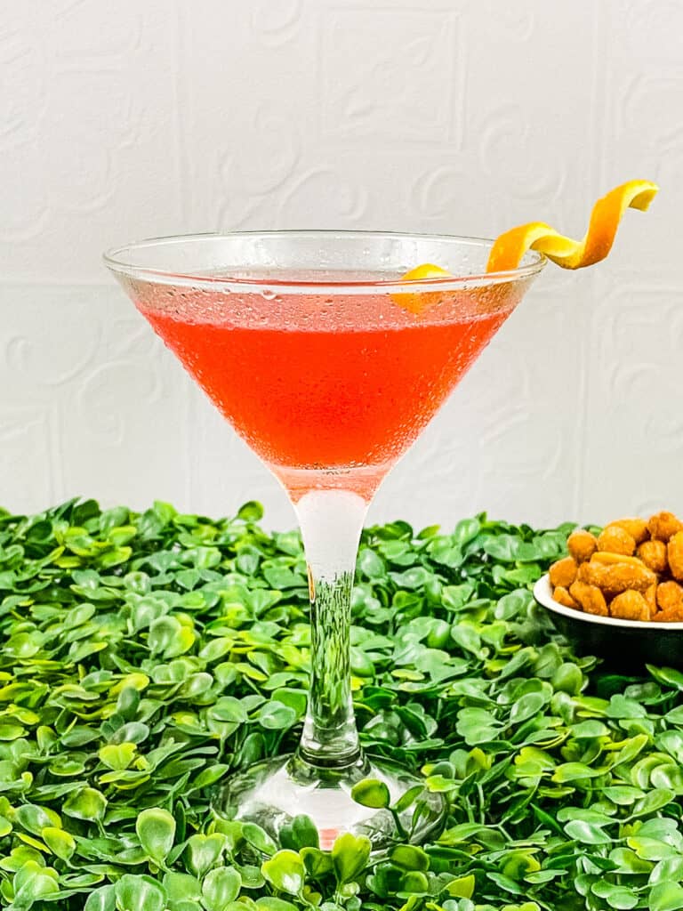 A delicious cosmopolitan cocktail with an orange twist, standing on a bed of clover.