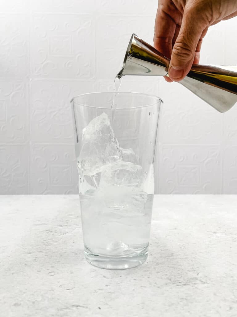 Adding vodka to a cocktail shaker filled with ice cubes.