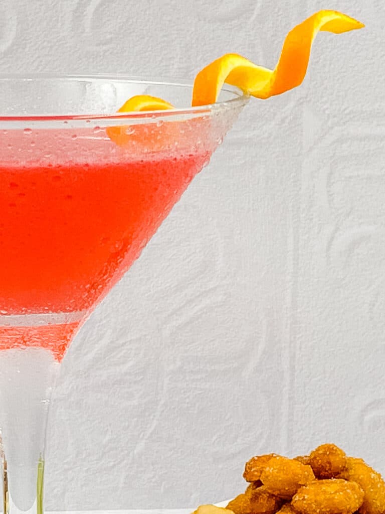 Partial shot of a cosmopolitan cocktail with an orange twist.