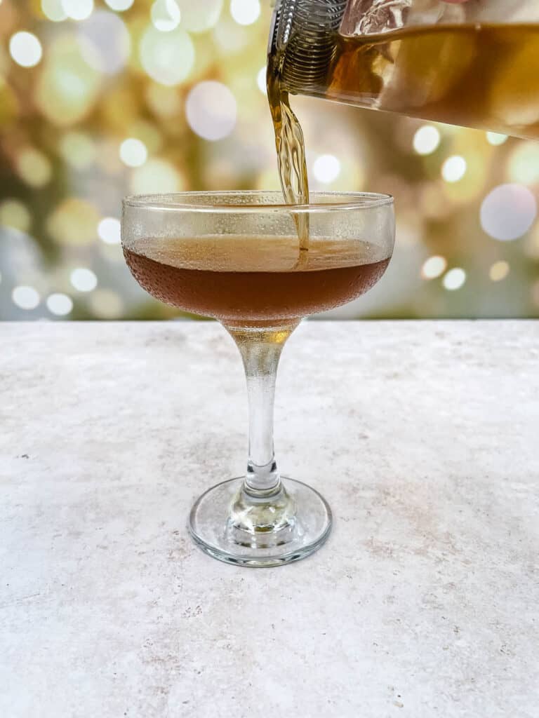 Someone pouring Manhattan drink into a cocktail glass.