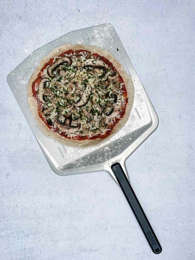 Mushroom pizza on a pizza peel ready to cook.