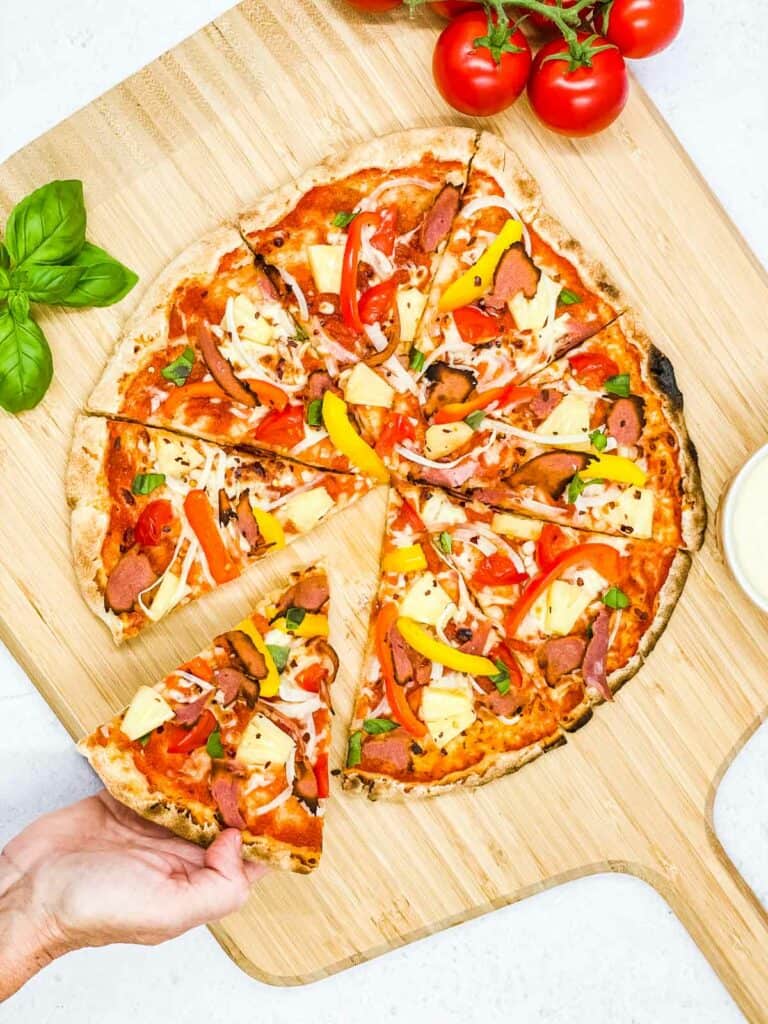 Someone helping themselves to a slice of veggie Hawaiian pizza.