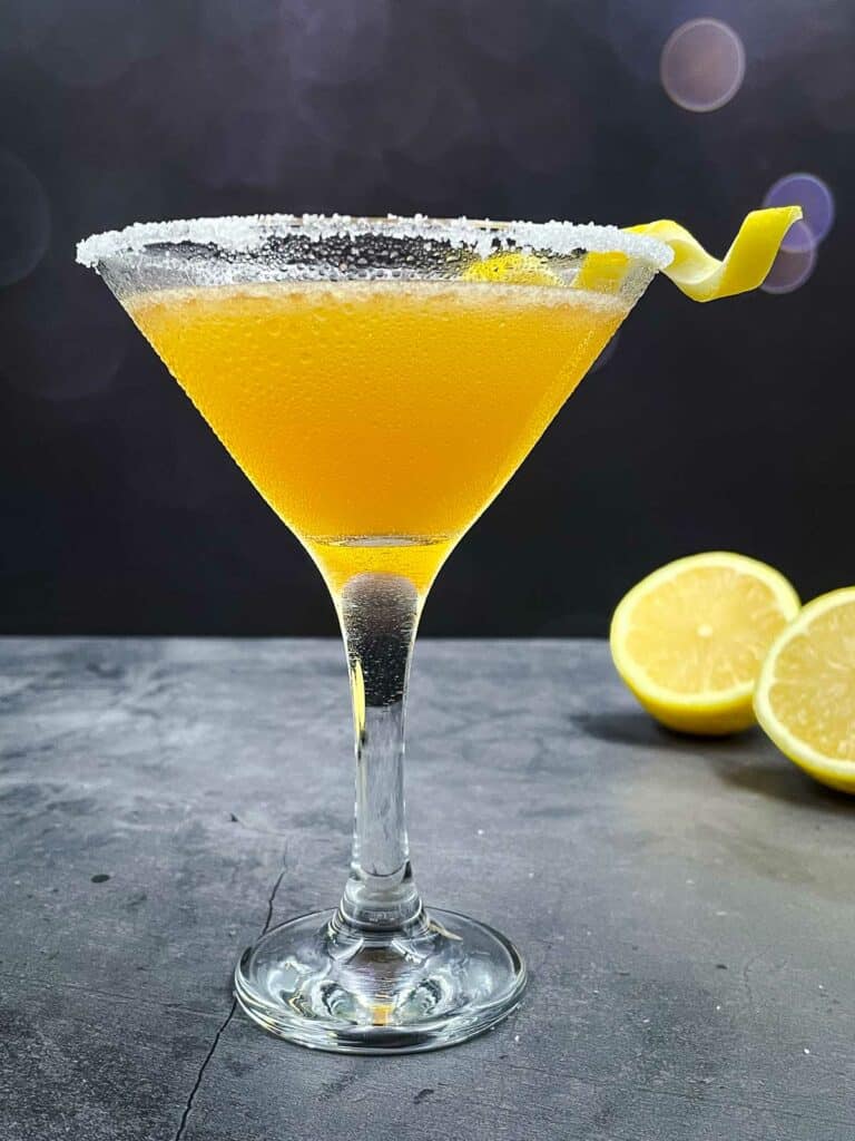 A stunning bright yellow sidecar cocktail with a lemon twist and fresh lemons in the background.