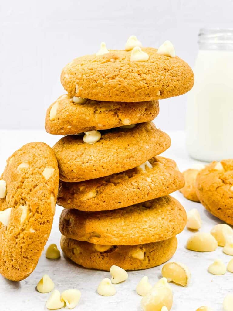 White chocolate macadamia nut cookies in a stack with chocolate chips and nuts around them.