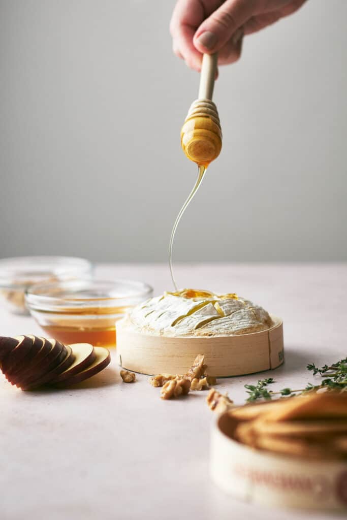 Someone drizzling honey on baked brie.