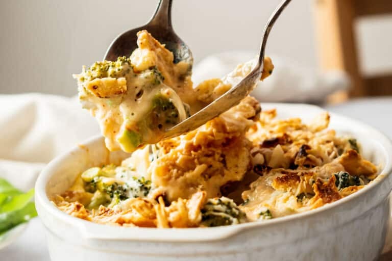 A serving spoon lifts a portion of cheesy broccoli casserole from a white baking dish.