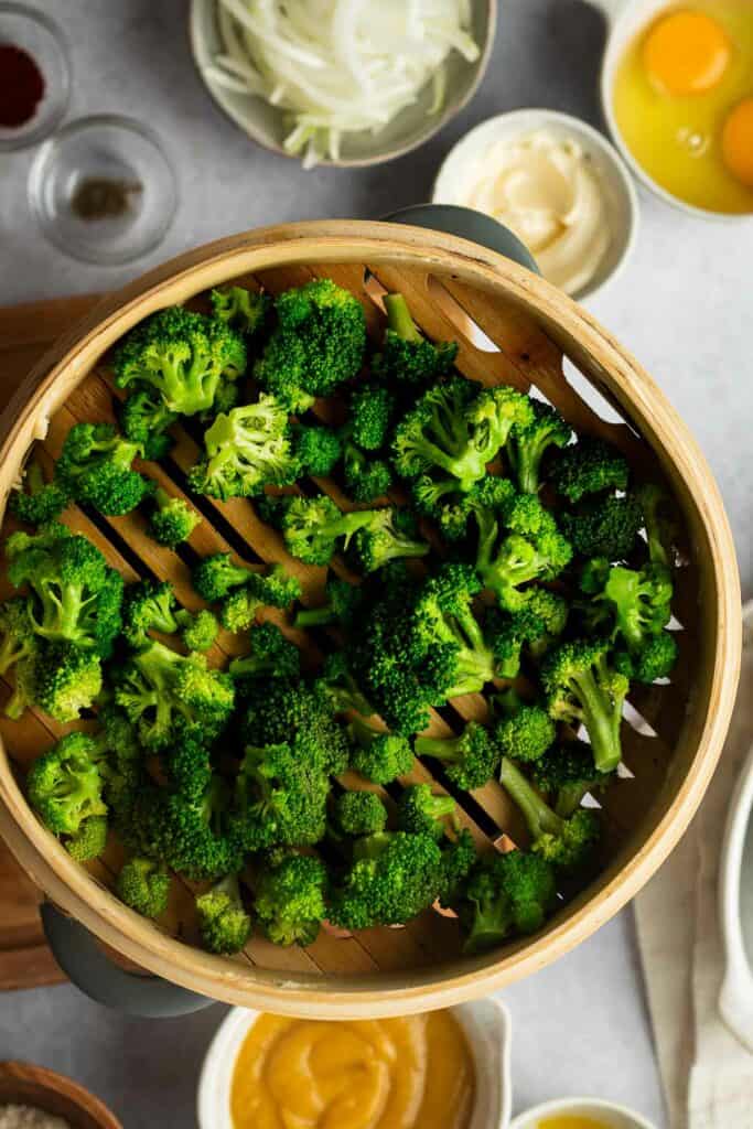 Broccoli florets steaming in a bamboo steamer.