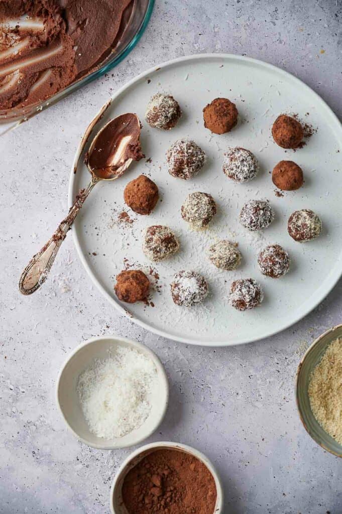 Freshly made chocolate truffles on a plate with a chocolaty spoon on the side.