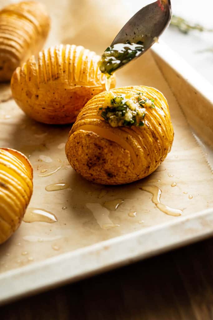Removing baked potato from oven and spooning the butter oil sauce on the potatoes.