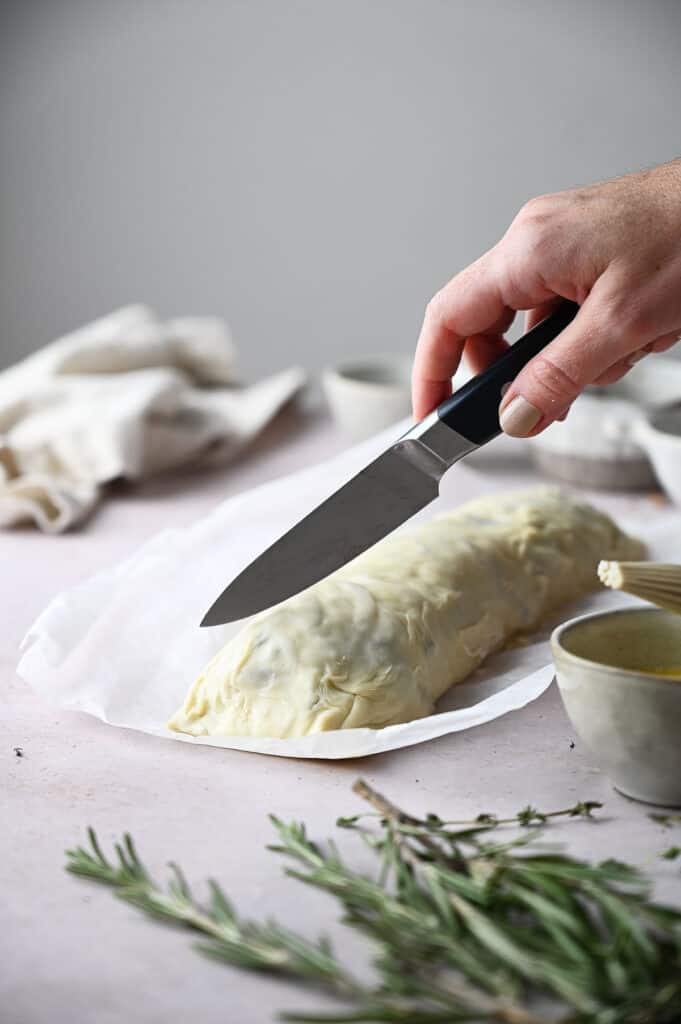 Someone scoring the top of the mushroom wellington with a sharp knife.