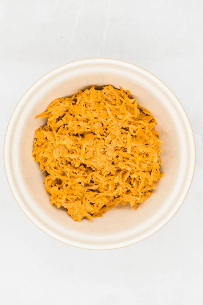 Shredded sweet potato mixed with flour and spice mixture in a large mixing bowl.