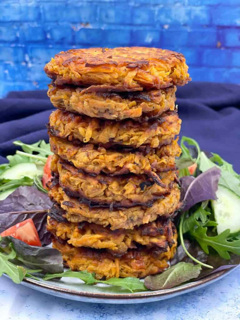 A stack of sweet potato fritters on a plate with salad around them.