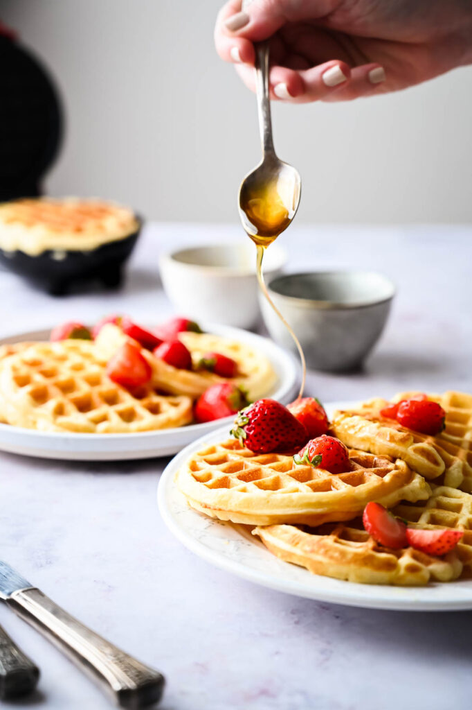 Drizzling honey over waffles with strawberries on.