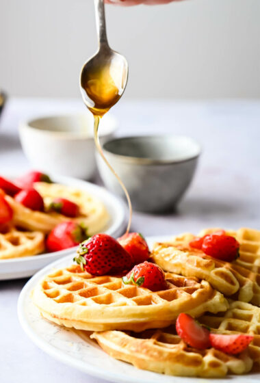 Someone drizzling honey over homemade waffles.
