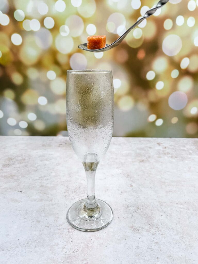 Adding a soaked sugar cube to a chilled champagne glass.