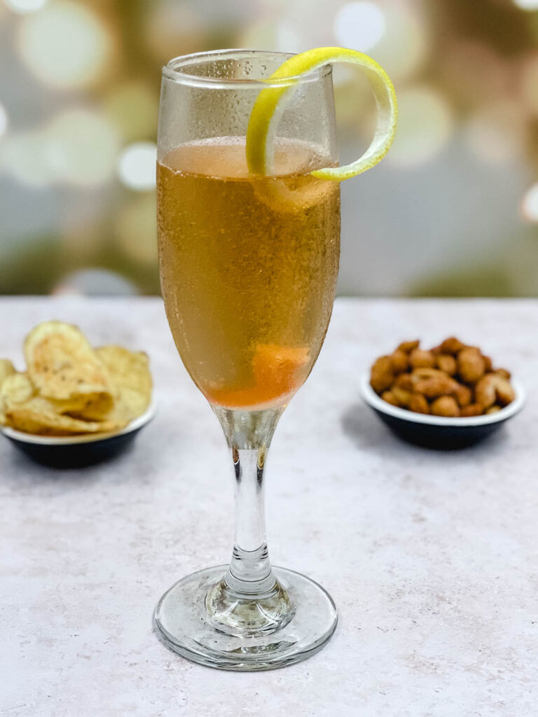 A freshly made champagne cocktail garnished with a swirl of lemon peel.