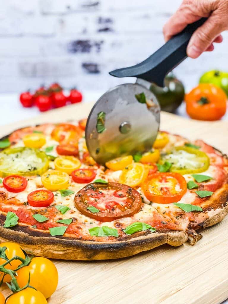 Someone cutting a tomato pizza with a pizza cutter.
