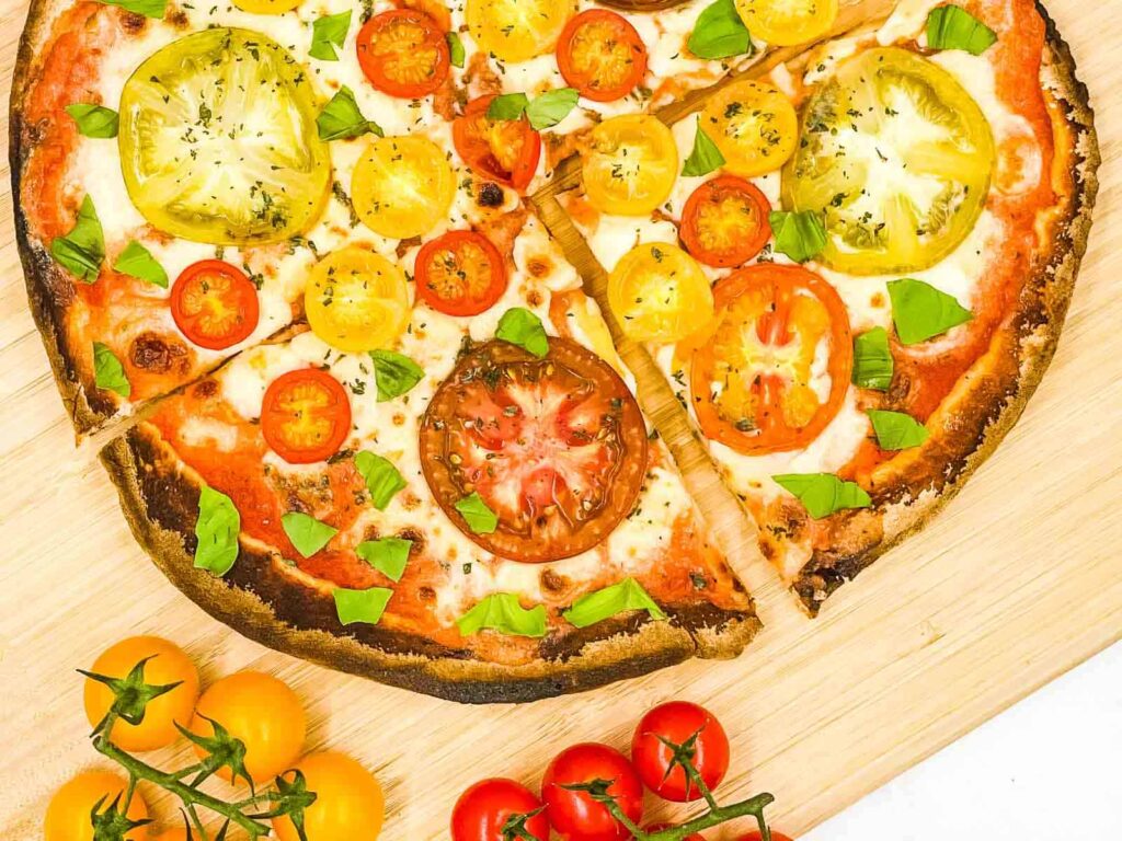 Tomato pizza on a board with vine tomatoes next to it.