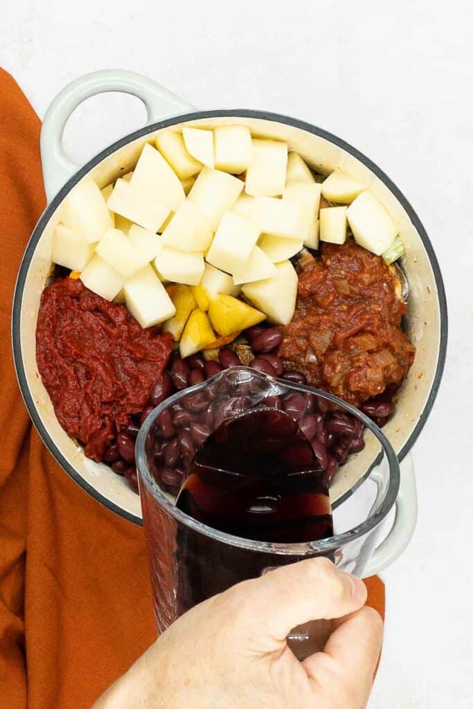 Adding red wine on top of vegetables.