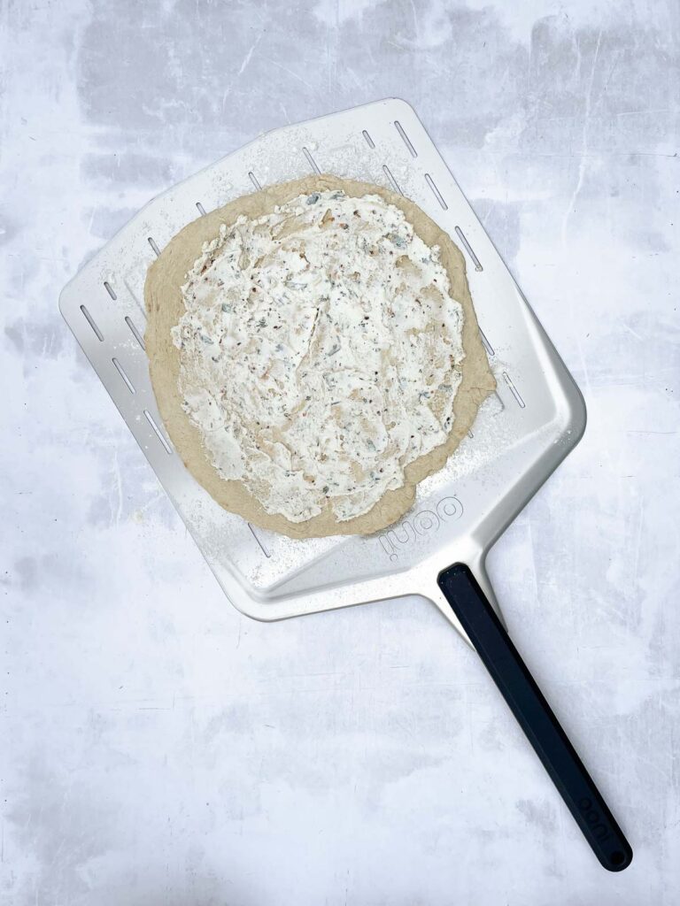 Pizza crust with ricotta cheese spread over it.