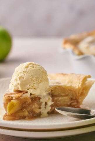 A mouthwatering slice of apple pie with a dollop of vanilla ice cream on top of it.