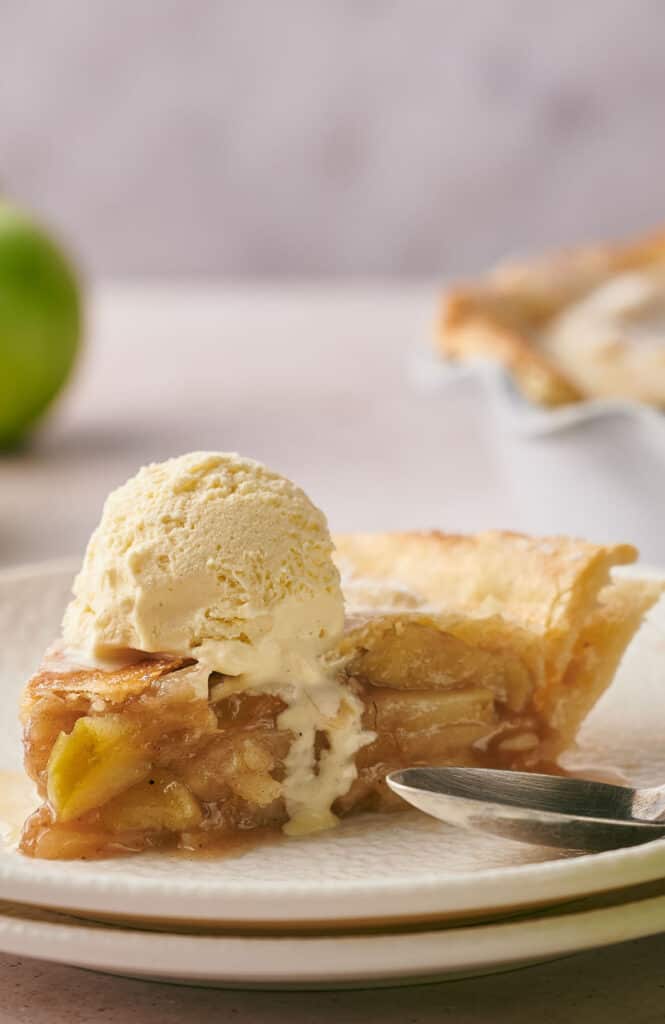 A mouthwatering slice of apple pie with a dollop of vanilla ice cream on top of it.