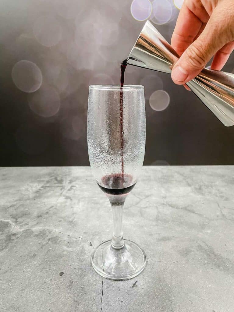 Pouring crème de cassis into a champagne flute.