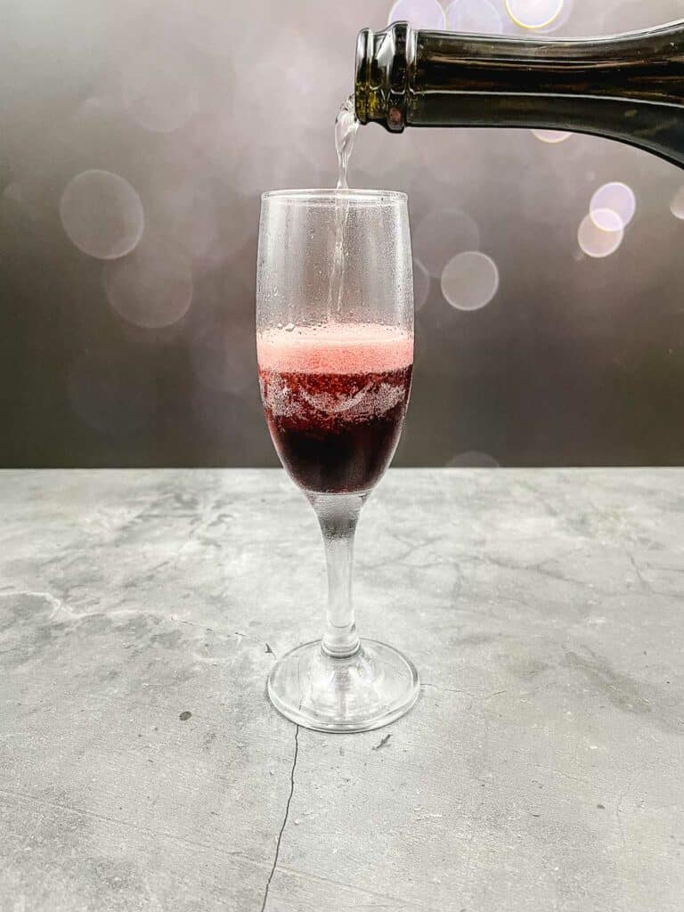 Pouring champagne or sparkling wine into champagne flute with crème de cassis in.