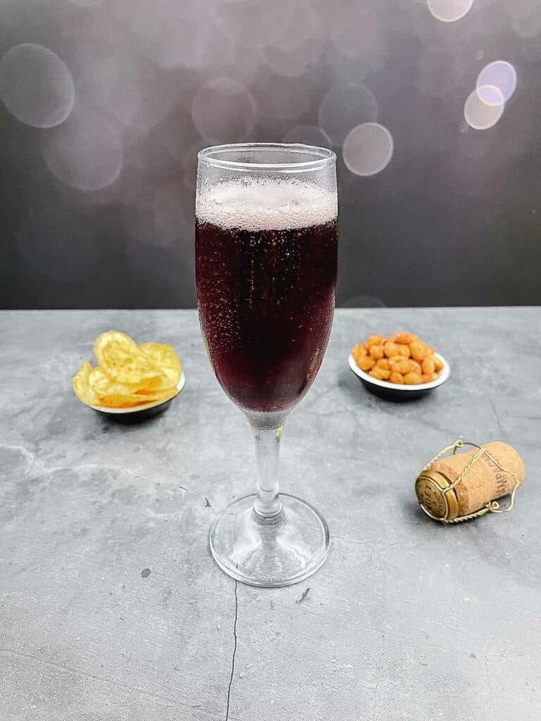 A glass of kir royale with a cork on the floor and bar snacks.