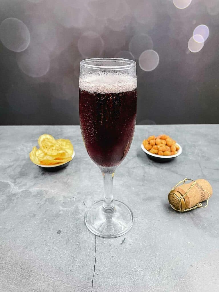 A glass of kir royale with a cork on the floor and bar snacks.
