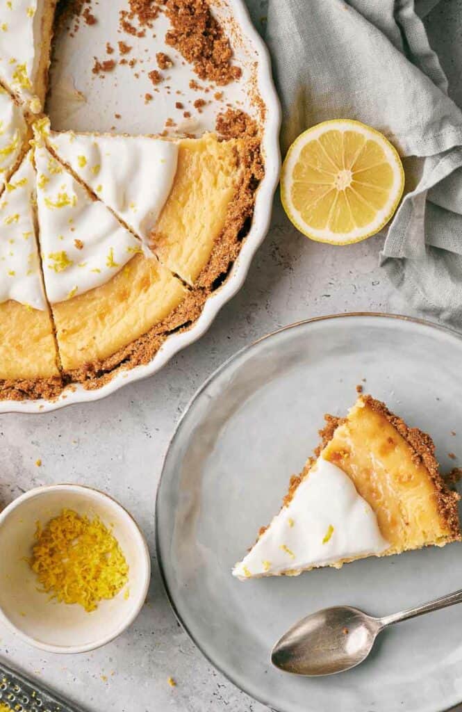 A slice of lemon pie and a partially eaten pie in a pie dish.