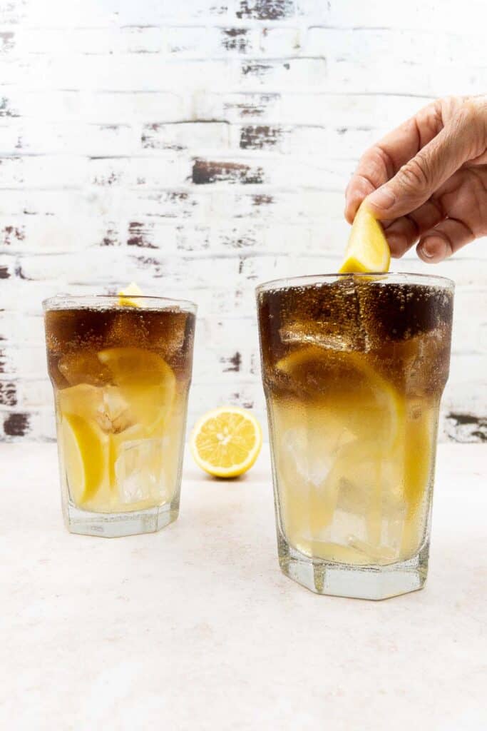Someone garnishing a Long Island iced tea with a lemon wedge.
